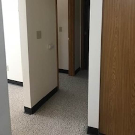 a hallway with a white wall and a brown door.