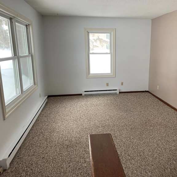 a room with a carpeted floor, a window, and a bench.