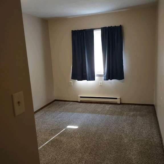 a room with a carpeted floor, a window with black curtains, and a wall-mounted air conditioning unit.
