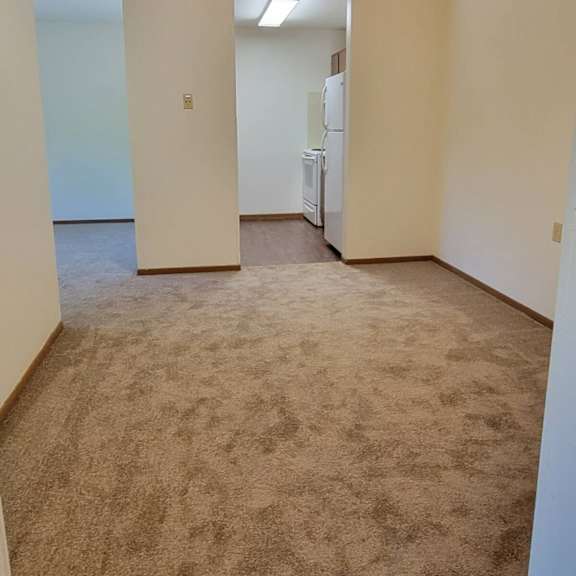 a carpeted room with a refrigerator in the corner.