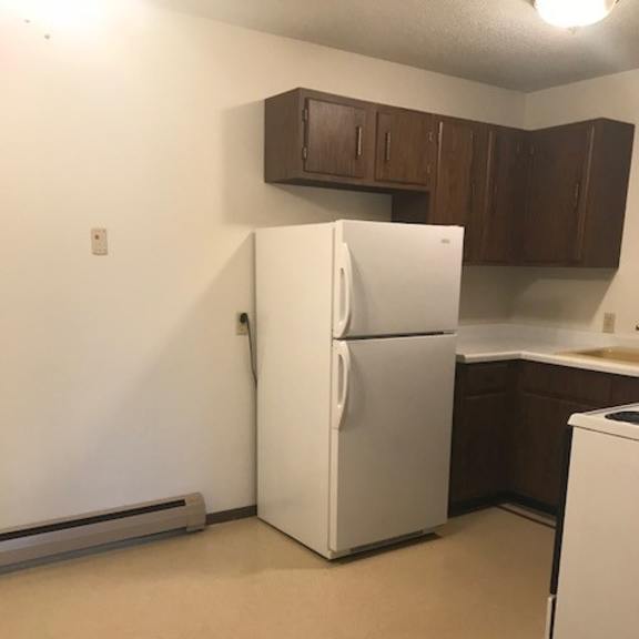 a white refrigerator stands in a kitchen with brown cabinets.