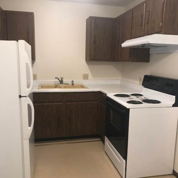 a white refrigerator stands next to a white stove in a kitchen with brown cabinets.