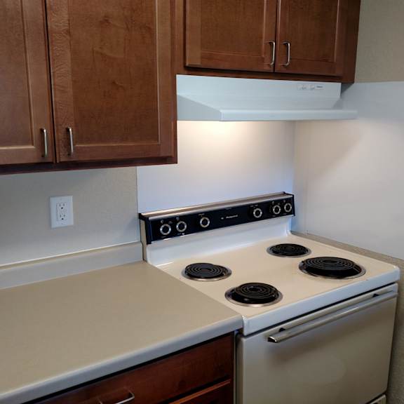 a white stove with four burners is in a kitchen with wooden cabinets.