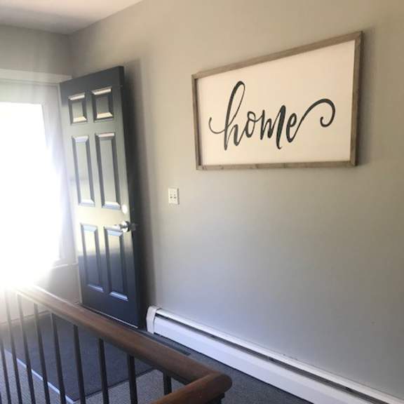 a black door with a white frame and a white wall with a black framed sign that says home.