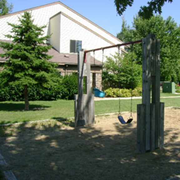 a swing set in a sandy area in front of a building.
