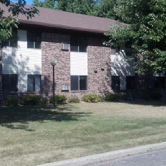 a brown and white building with a green lawn in front.