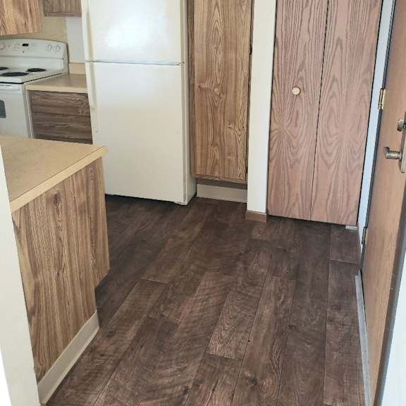 a kitchen with a white fridge and wooden floors.