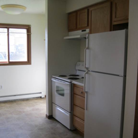 a white refrigerator in a kitchen with a white wall and a window.