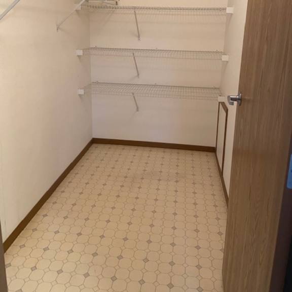 empty walk in closet with tile floor and white shelving.