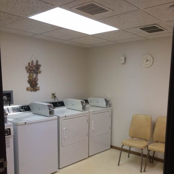a laundry room with a washer and dryer, a clock, and two chairs.