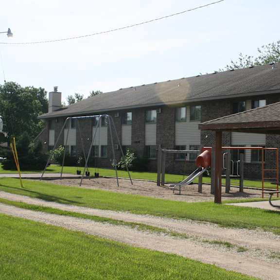 a playground with a swing set and a slide in front of a building.