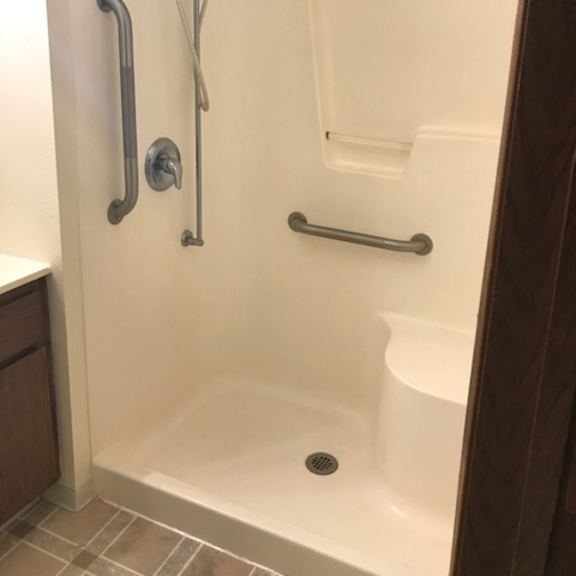 a white shower stall with a silver shower head and grab bars.