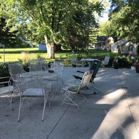 a patio with chairs and a table is surrounded by trees.