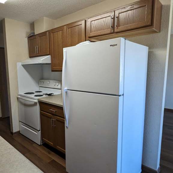 a white refrigerator stands in a kitchen with wooden cabinets and a stainless steel sink.