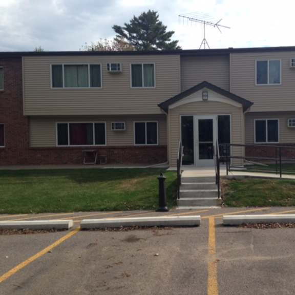a building with a grey facade and a black door is surrounded by a parking lot.