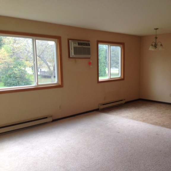 a room with a carpeted floor, two windows, and a chandelier.