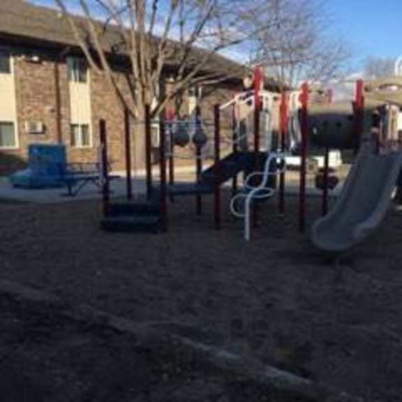 a playground with a slide and swings in the foreground and apartment buildings in the background.