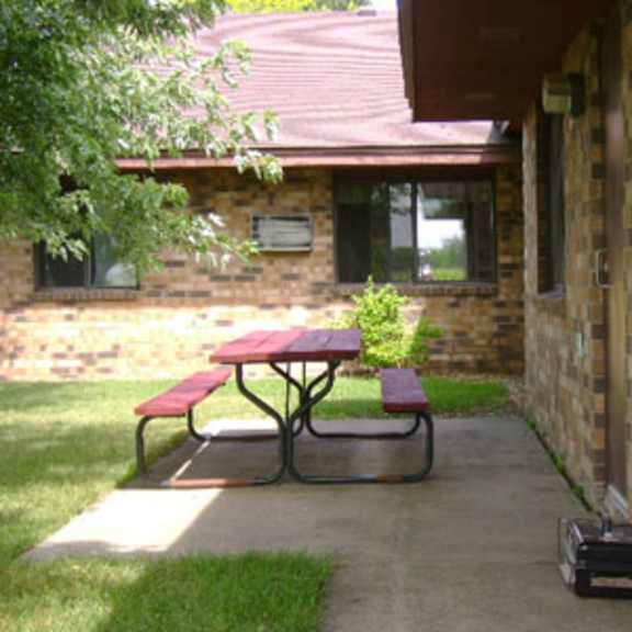 a picnic table is on a concrete patio outside a brick building.