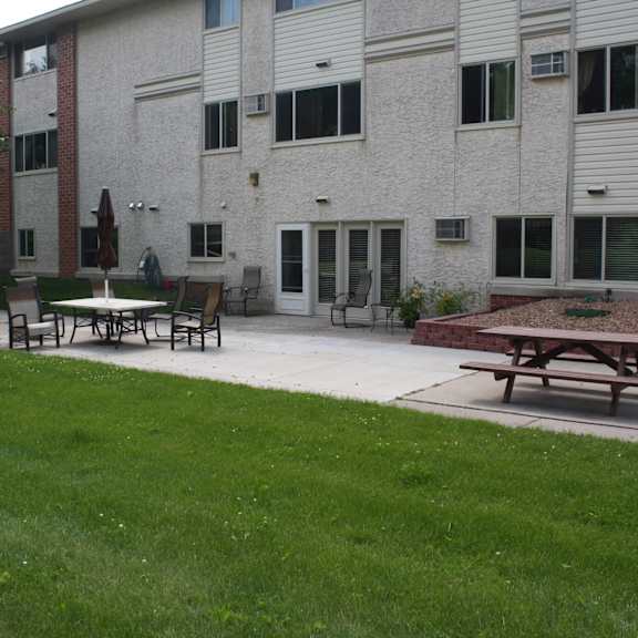 a grassy area in front of a building with a picnic table and chairs.