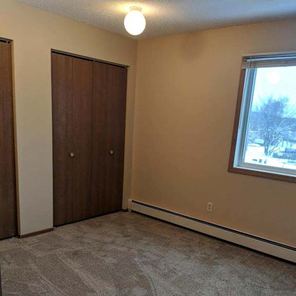 a room with a carpeted floor, a window, and two doors.