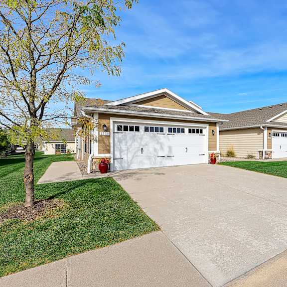 a house with a white garage door is surrounded by a green lawn and a clear blue sky.