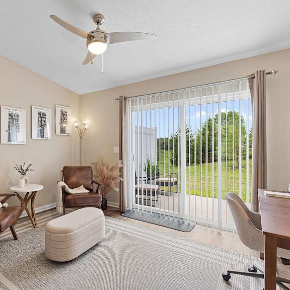 a living room with a ceiling fan and a view of a green lawn outside.