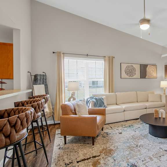 a living room with a white couch, brown chairs, and a rug.