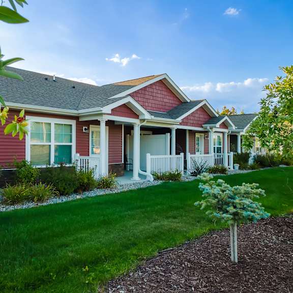 a red house with a white picket fence and a small tree in front.