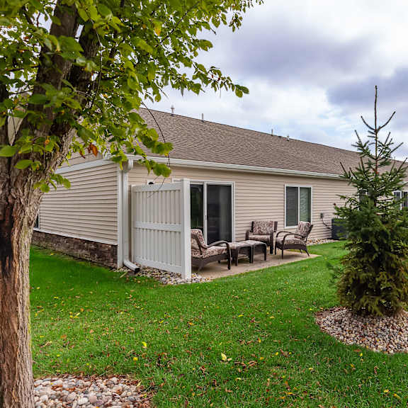 a house with a brown roof and a grey exterior is surrounded by a green lawn and trees.