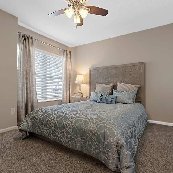 a bedroom with a bed, a ceiling fan, and a painting on the wall.