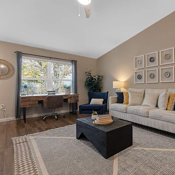 a living room with a white couch, a black coffee table, and a large window with a view of trees.