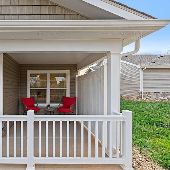 a small porch with a white railing and a red chair.