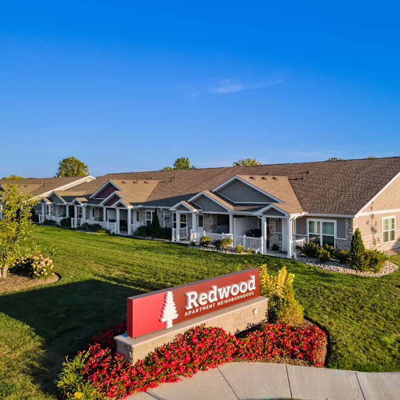 a redwood sign is in front of a building with a lawn and flowers.