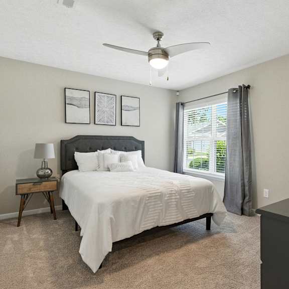 a bedroom with a large bed, a nightstand with a lamp, and a ceiling fan.