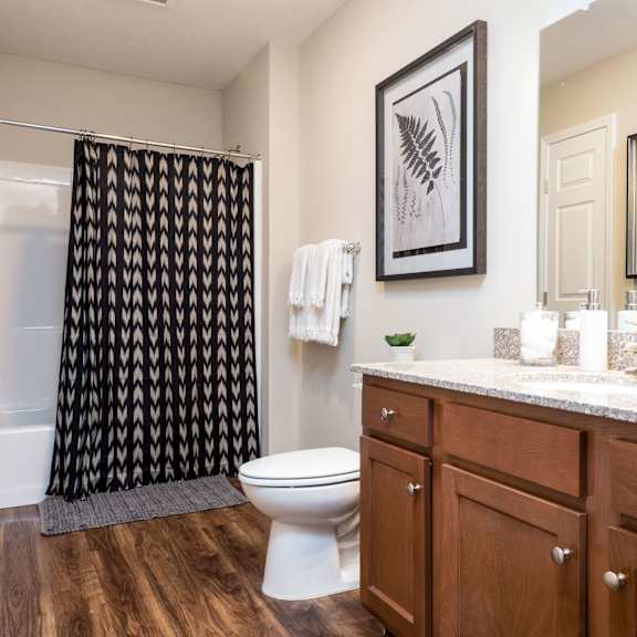 a bathroom with a toilet, a shower curtain, and a counter with a sink and a potted plant.