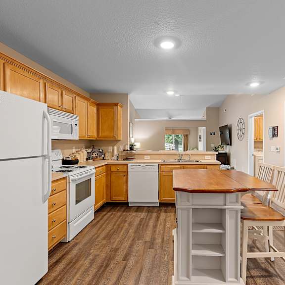 a kitchen with a white refrigerator, wooden cabinets, and a wooden island with a chair.