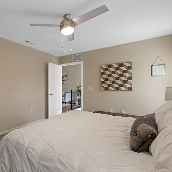 a bedroom with a bed, a ceiling fan, and a checkerboard patterned picture on the wall.