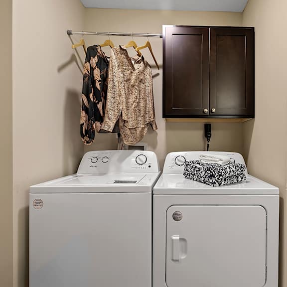 a laundry room with a white washer and dryer, a towel, and clothes hanging up.
