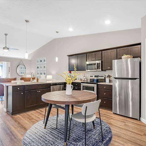 a modern kitchen with a round wooden table and a stainless steel refrigerator.