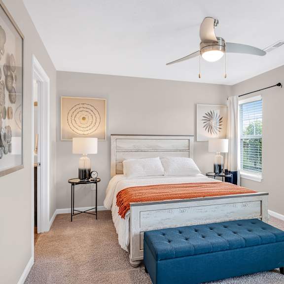 a bedroom with a bed, a bench, and a ceiling fan.