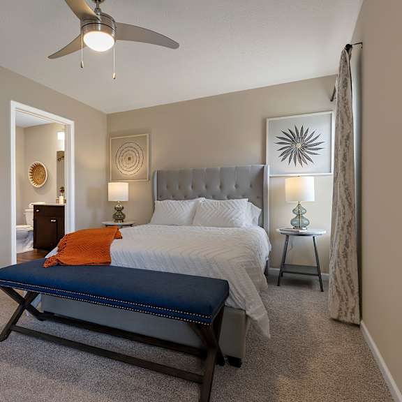 a bedroom with a bed, a bench, and a ceiling fan.