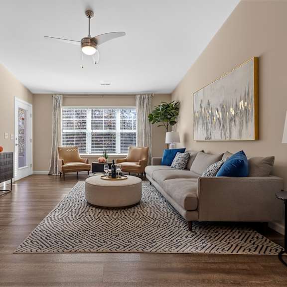 a living room with a grey couch, a coffee table, a television, and a fan.
