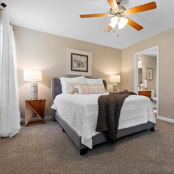a bedroom with a bed, a ceiling fan, and a nightstand with a lamp.