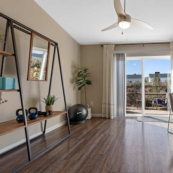 a room with a sliding glass door leading to a balcony, a chair, a desk, and a fan.