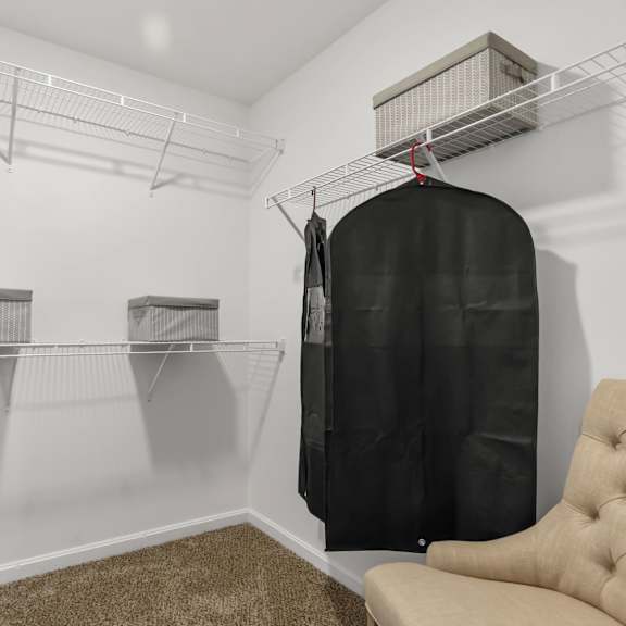 a room with a chair, a bag hanging on a rack, and a trash can.