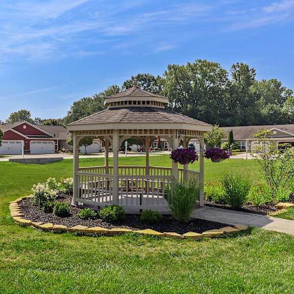 a gazebo is surrounded by a flower bed in a grassy area.