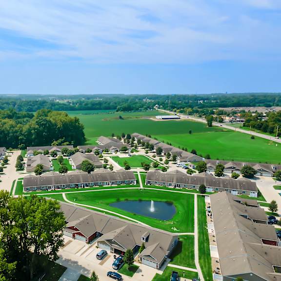 a bird's eye view of a residential neighborhood with houses, a pond, and a green field.