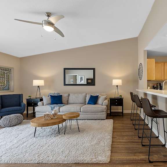 a living room with a white rug and a white couch with blue pillows.