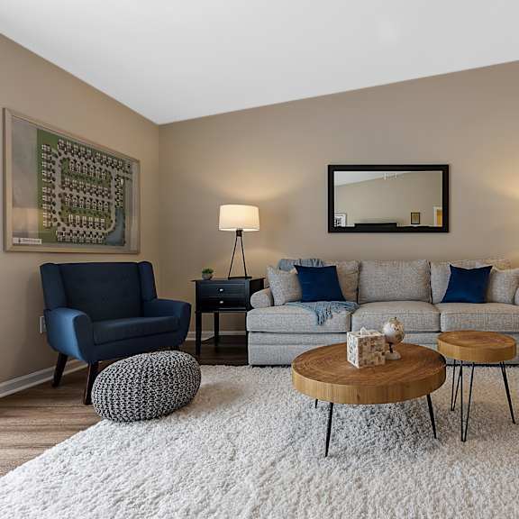 a living room with a grey couch, a blue chair, a wooden coffee table, and a mirror on the wall.