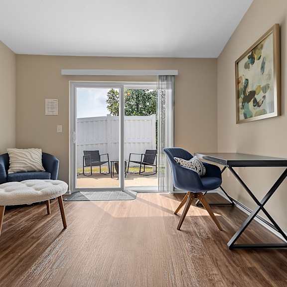 a room with a blue chair and a white chair with a round ottoman in front of a sliding glass door.